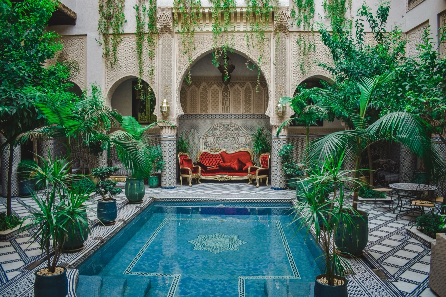 Lush planted inner courtyard with arches, palms, hanging greenery and a small turquoise plunge pool