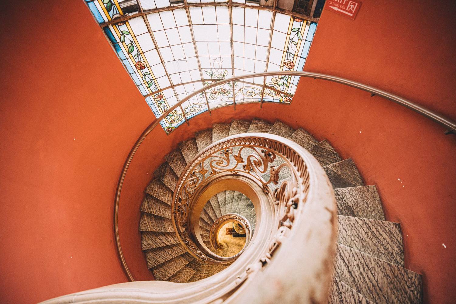 A stunning top-down view of a spiral staircase with intricate railing and stained glass ceiling.