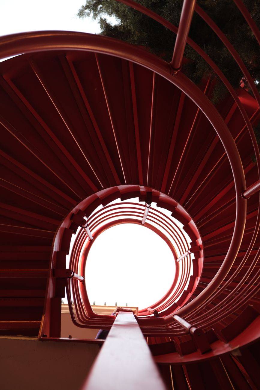 A mesmerizing view of a red spiral staircase seen from below, creating a dynamic abstract pattern.