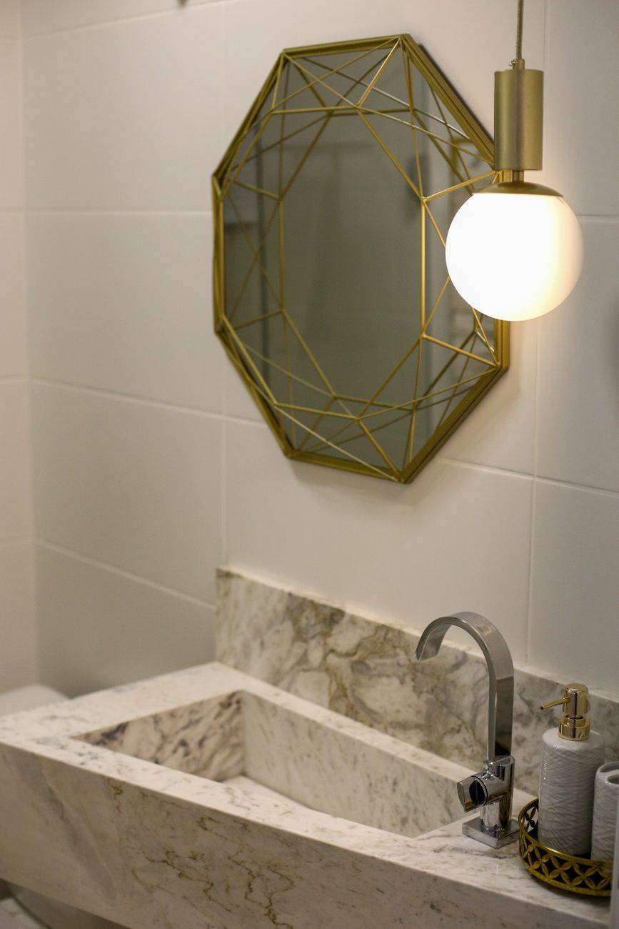 Stylish bathroom featuring a gold geometric mirror and marble sink with a hanging lamp.