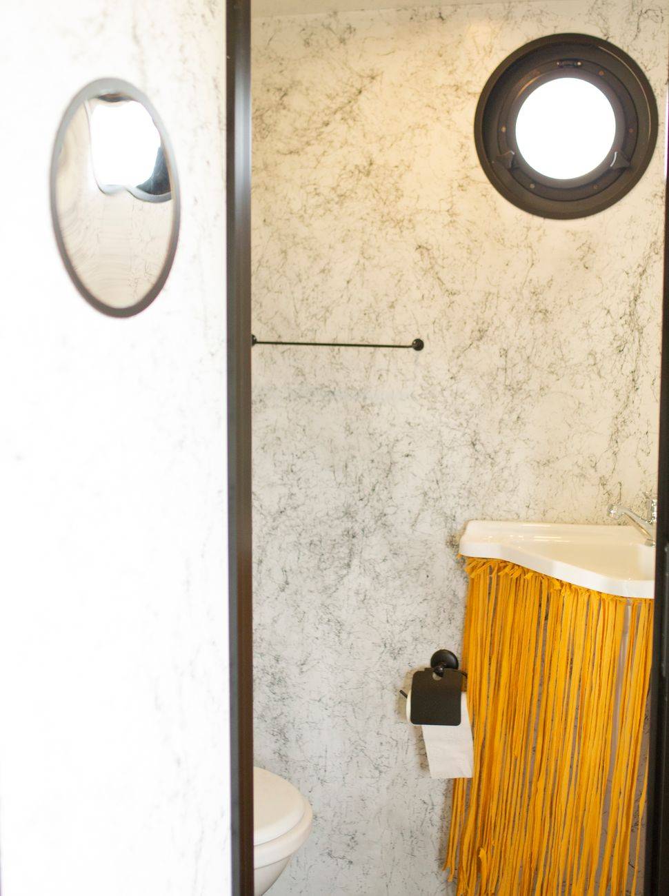 Stylish bathroom featuring a marble wall, round window, and unique fringe decor on the sink.