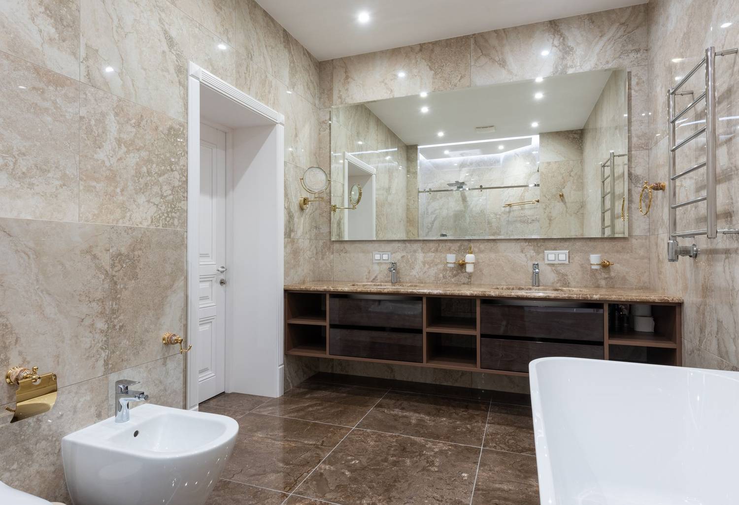 Interior of modern light bathroom with bidet next to bath and sinks with faucets on cabinet under mirror