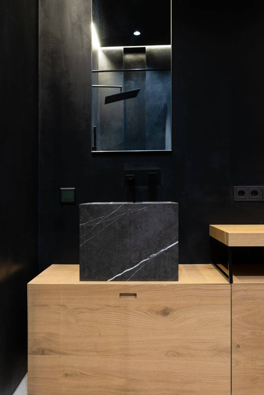 Interior details of modern bathroom with square black marble sink placed on wooden cabinet under mirror hanging on wall