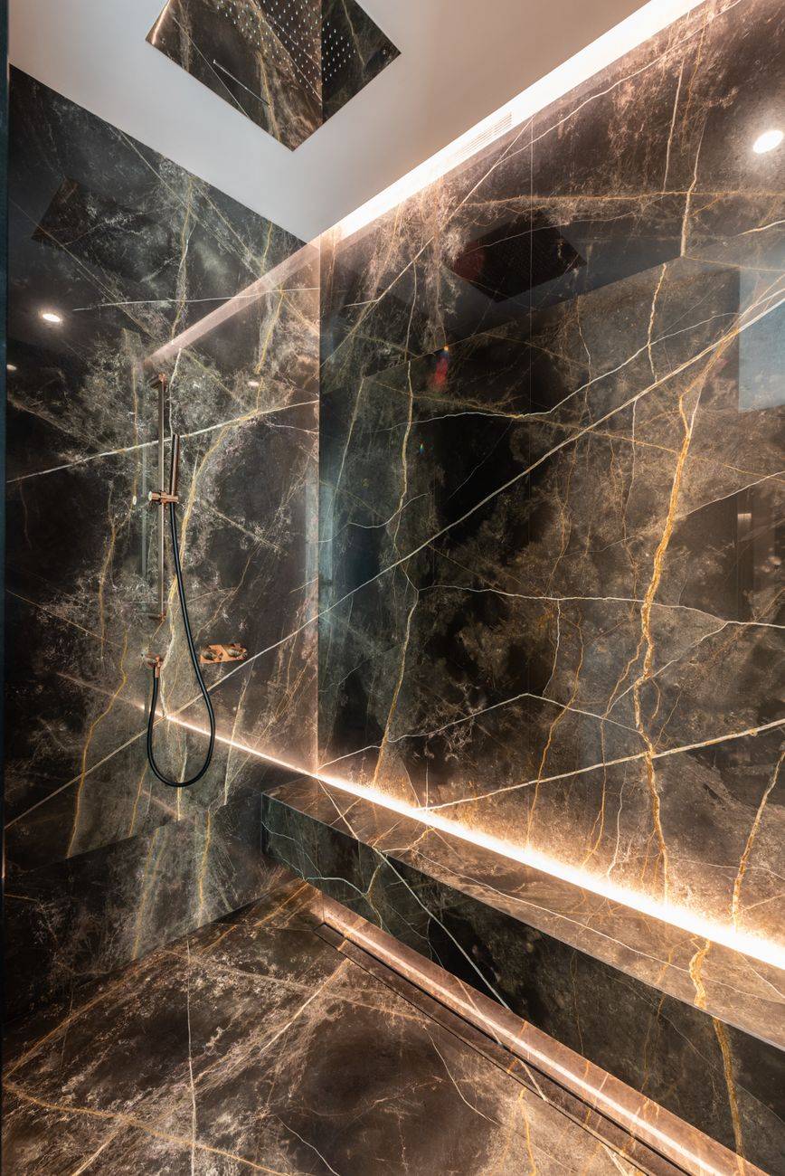 Interior design of bathroom with shower and marble walls illuminated with lamps in modern apartment