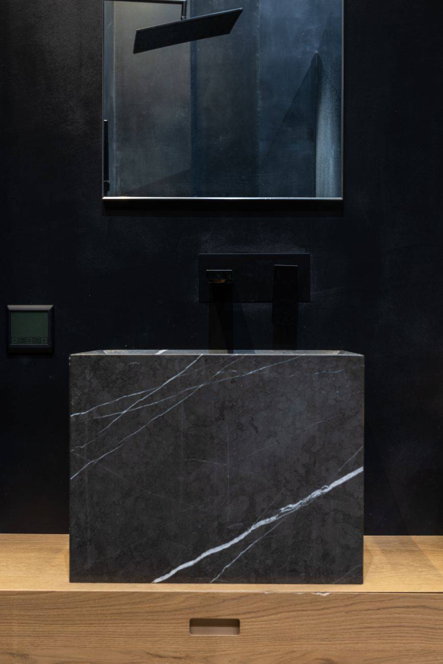 Creative black marble sink installed on wooden cupboard under mirror hanging on wall in modern minimalist styled bathroom