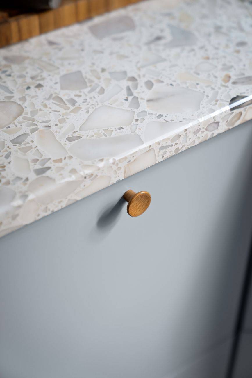 Close-up of a modern grey cabinet with a terrazzo marble top and simple wooden knob.