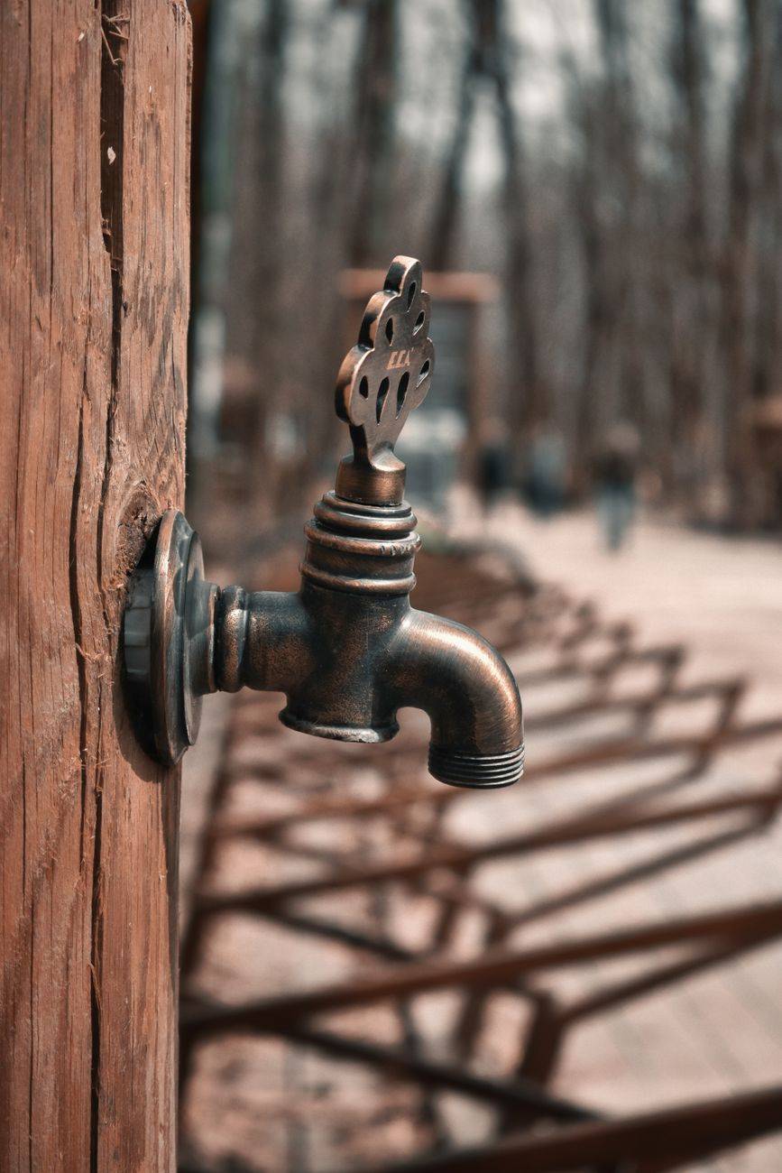 An antique brass water faucet on a wooden post with a blurred outdoor background.