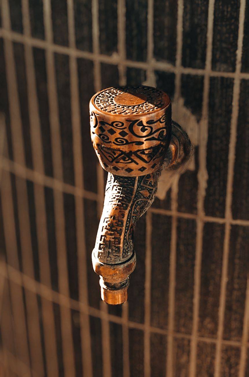 Detailed view of a beautifully carved metal tap with ornate patterns, capturing light indoors.