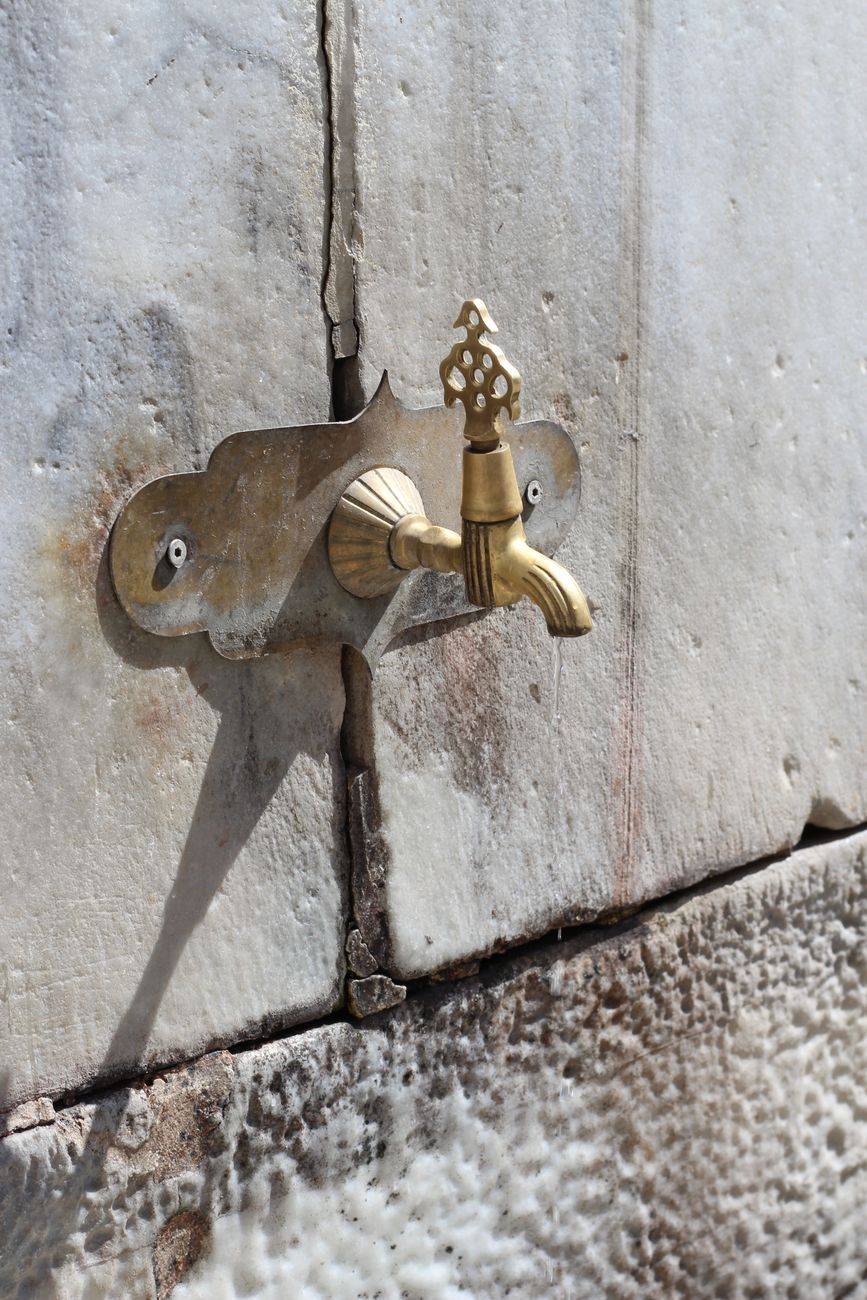 Close-up of a decorative brass tap on a textured stone wall, casting a shadow.