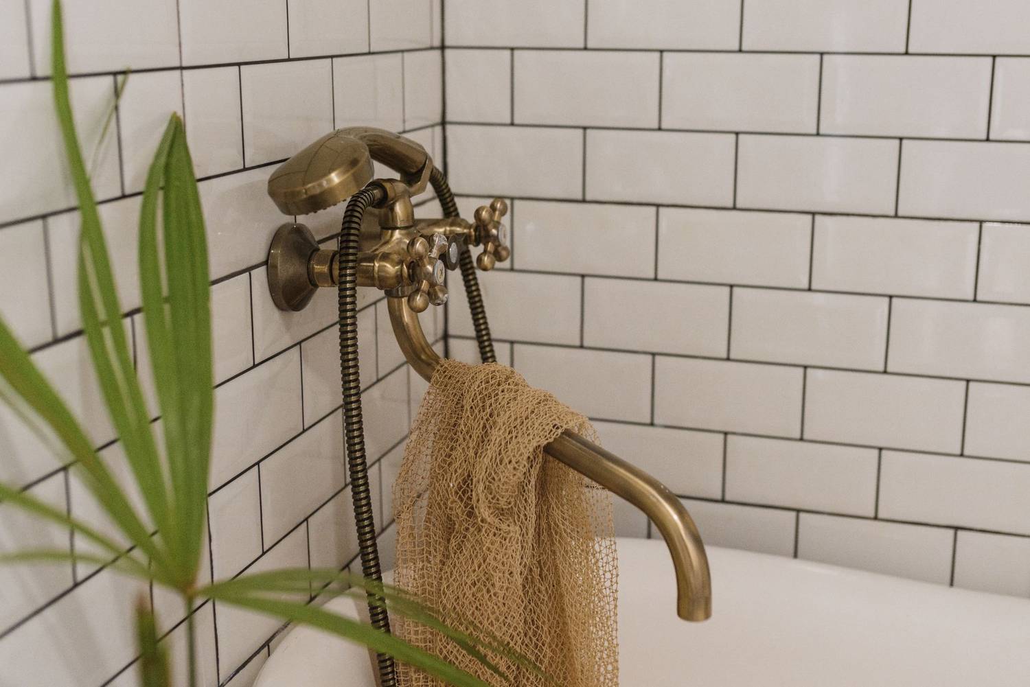 Stylish vintage brass faucet in a white tiled bathroom interior with a plant accent.