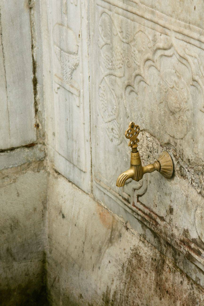 Antique brass faucet against an intricately carved stone wall, depicting classic architecture.