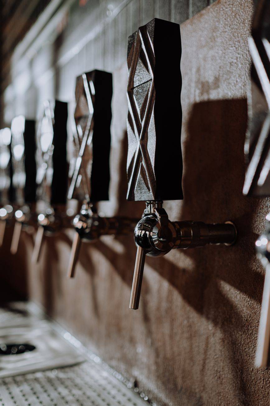 A close-up of beer taps in a dimly lit pub with a focus on the metal and wooden handles.