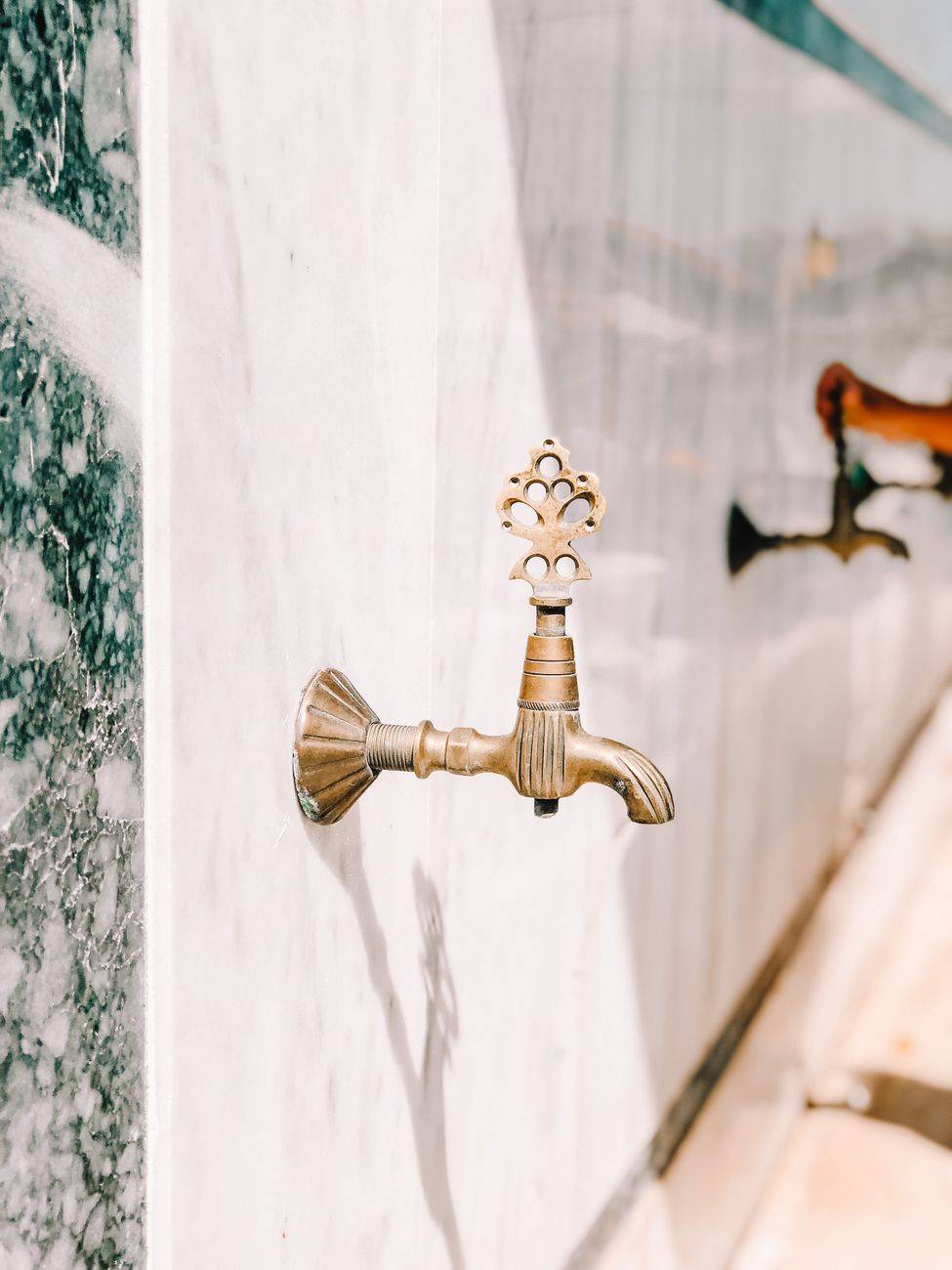 Close-up of a vintage brass faucet on a decorative marble wall outdoors.
