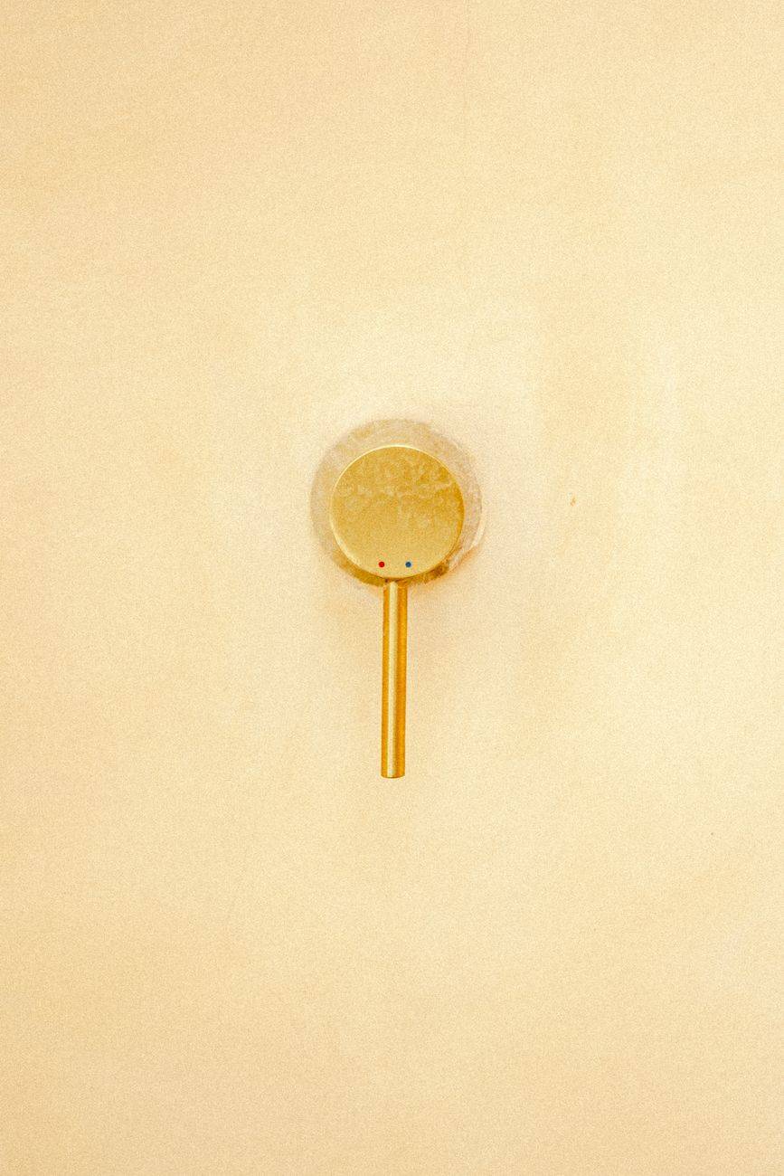 A sleek gold water faucet set against a smooth beige wall, exuding simplicity and elegance.