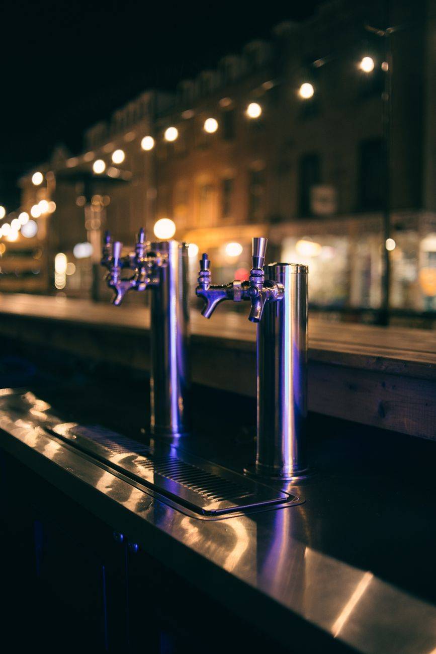 Close-up of beer taps at an outdoor bar with city lights at night.