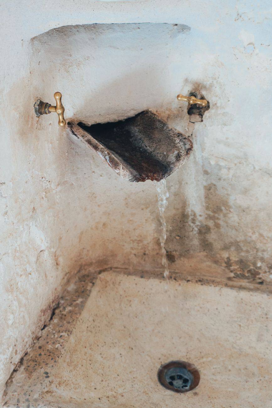 An image of a vintage faucet with water dripping into an old stone sink, creating a rustic atmosphere.