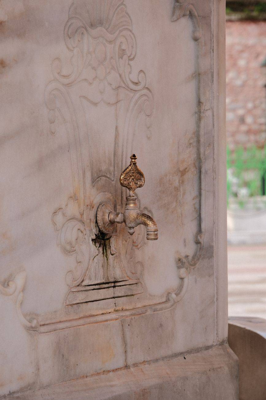 A detailed view of an ornate vintage water tap set into an intricately designed marble wall.
