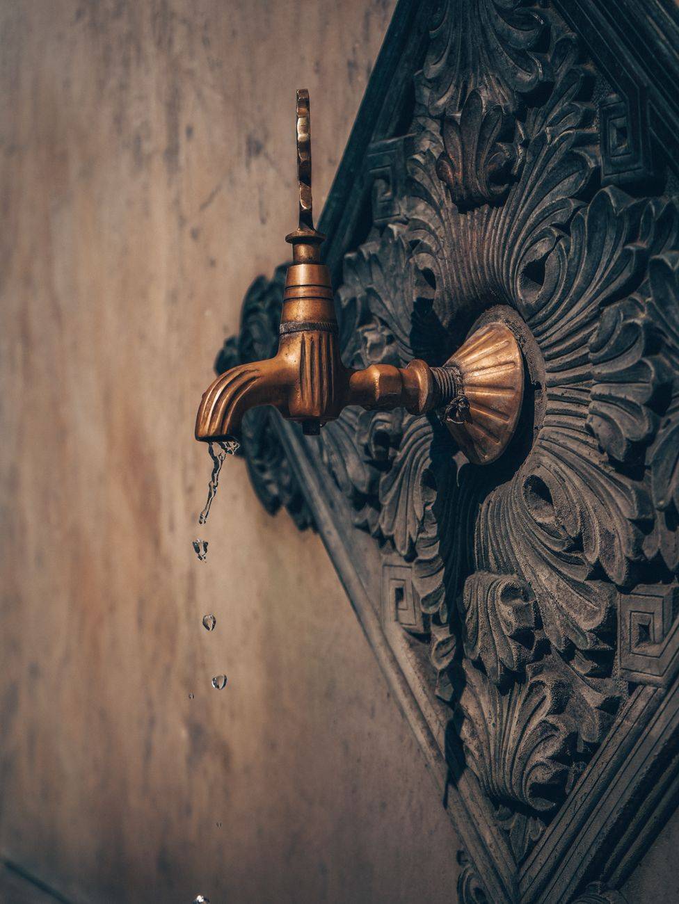 An ornate bronze tap on a decorative vintage background, dripping water.