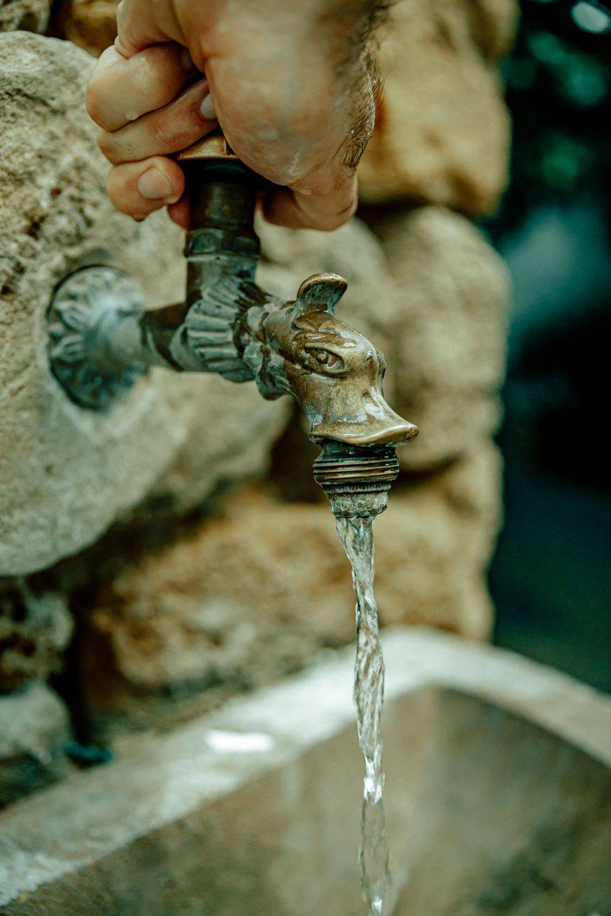 A vintage metal faucet with running water against a stone wall, depicting rustic charm.