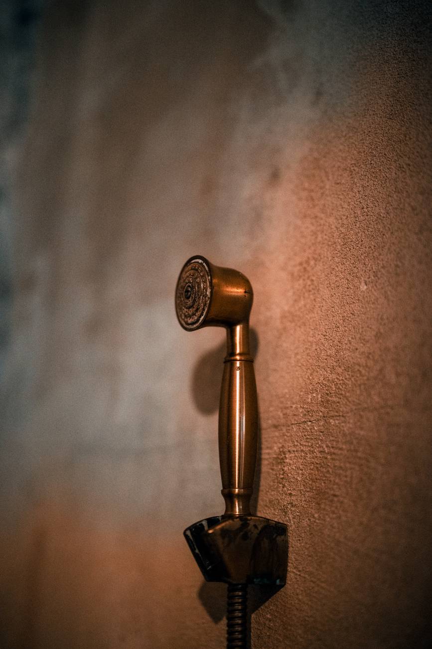 Close-up of a vintage brass shower head against a textured wall in Bangkok, Thailand.