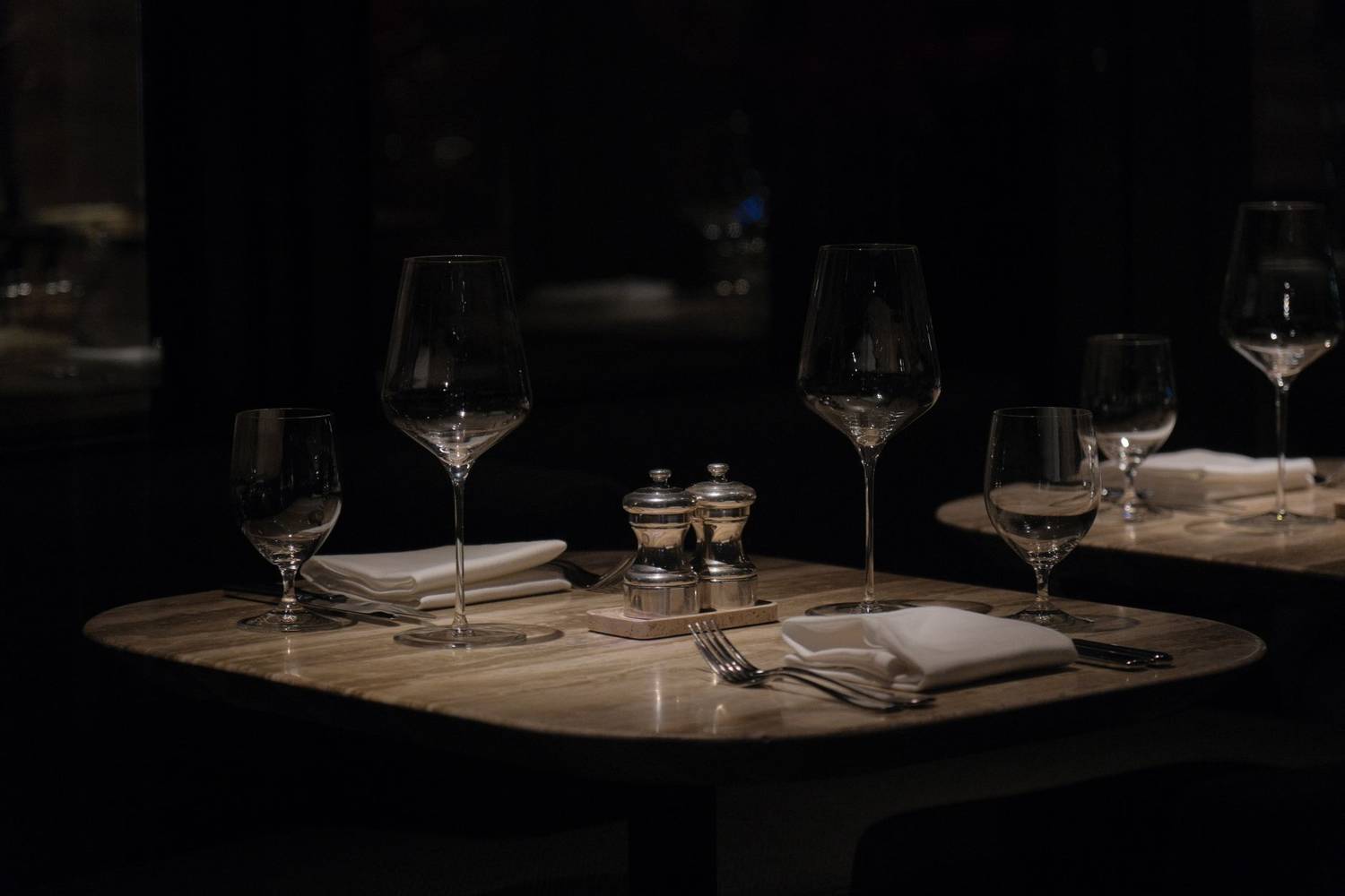 A dark, atmospheric restaurant table setup with wine glasses and napkins, creating a sophisticated ambiance.