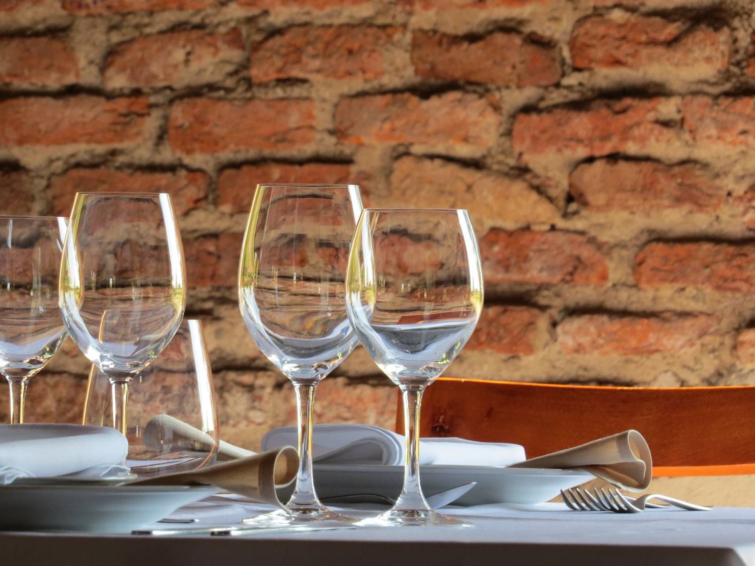 A refined table setup with wine glasses and plates against a rustic brick wall backdrop.