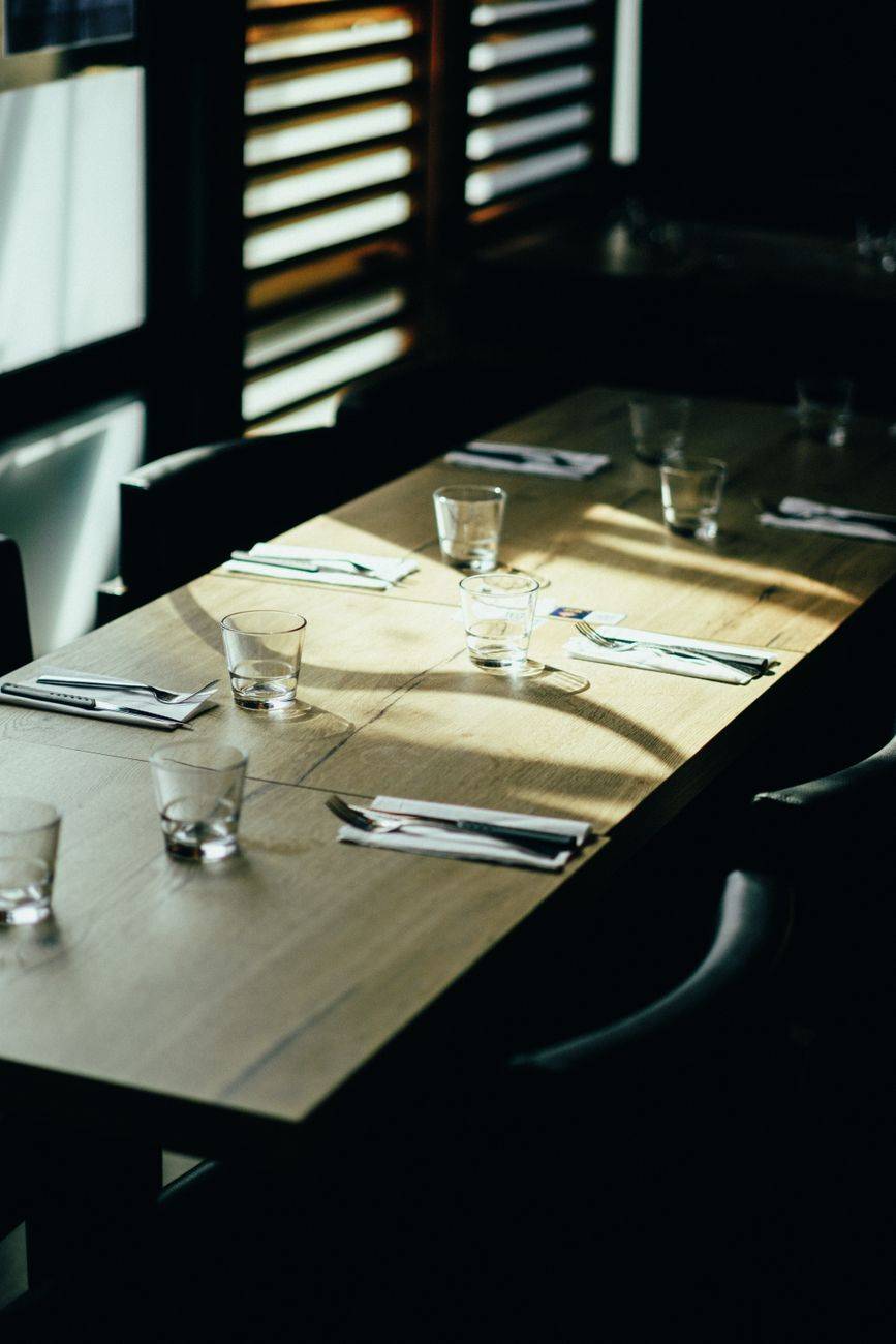 Sunlit table setting with glassware and utensils in a stylish restaurant interior.