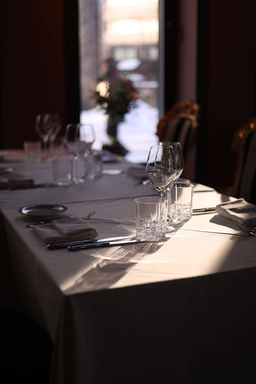Sunlit restaurant table elegantly set with wine glasses and white tablecloth.