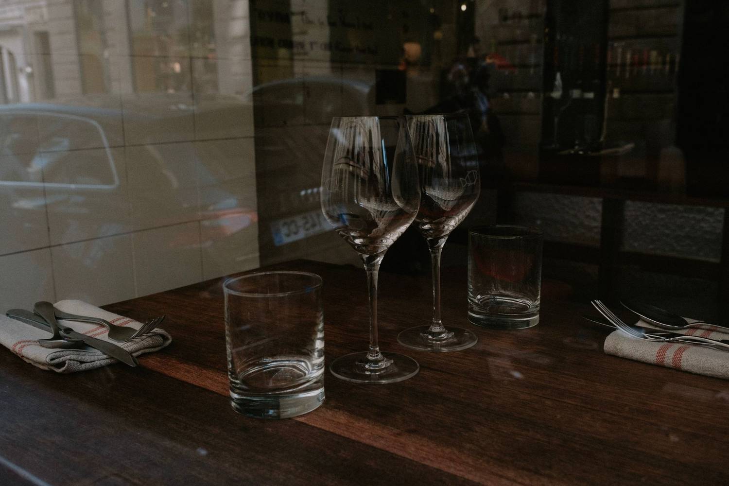 Wine glasses and cutlery on a wooden restaurant table.