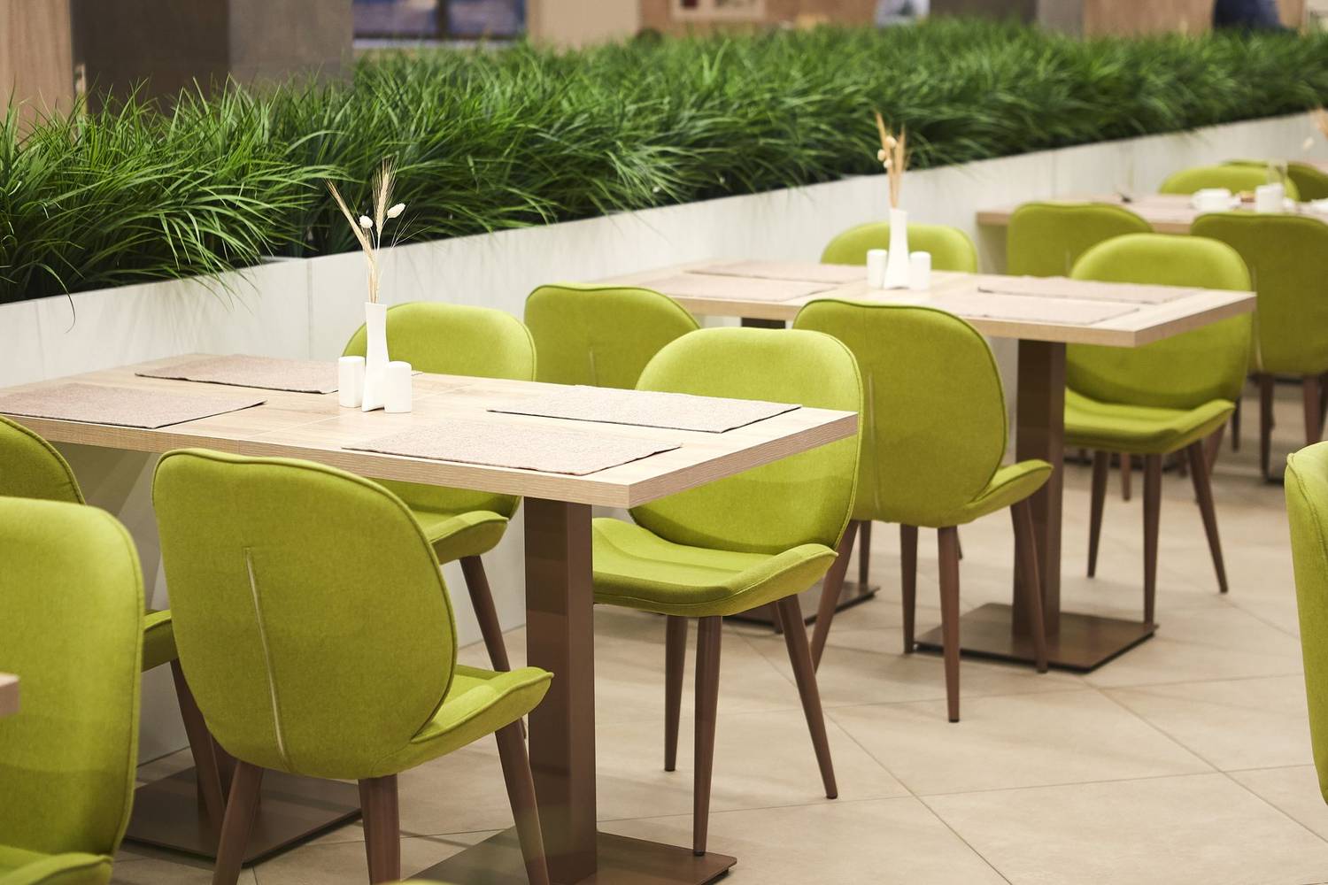 Contemporary dining area with green chairs and wooden tables indoors.