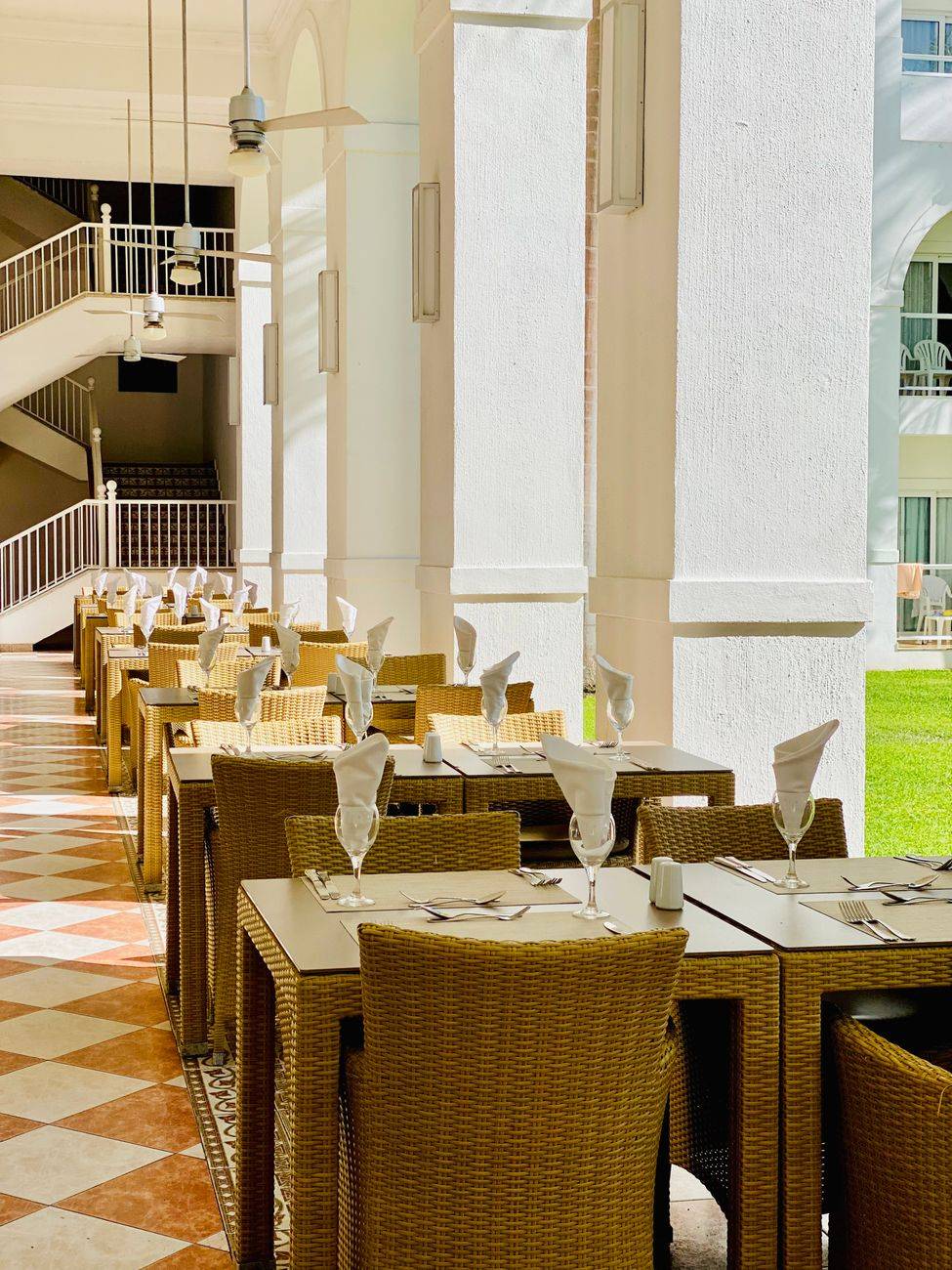 Brightly lit outdoor patio dining setup with wicker furniture in a luxury hotel setting.