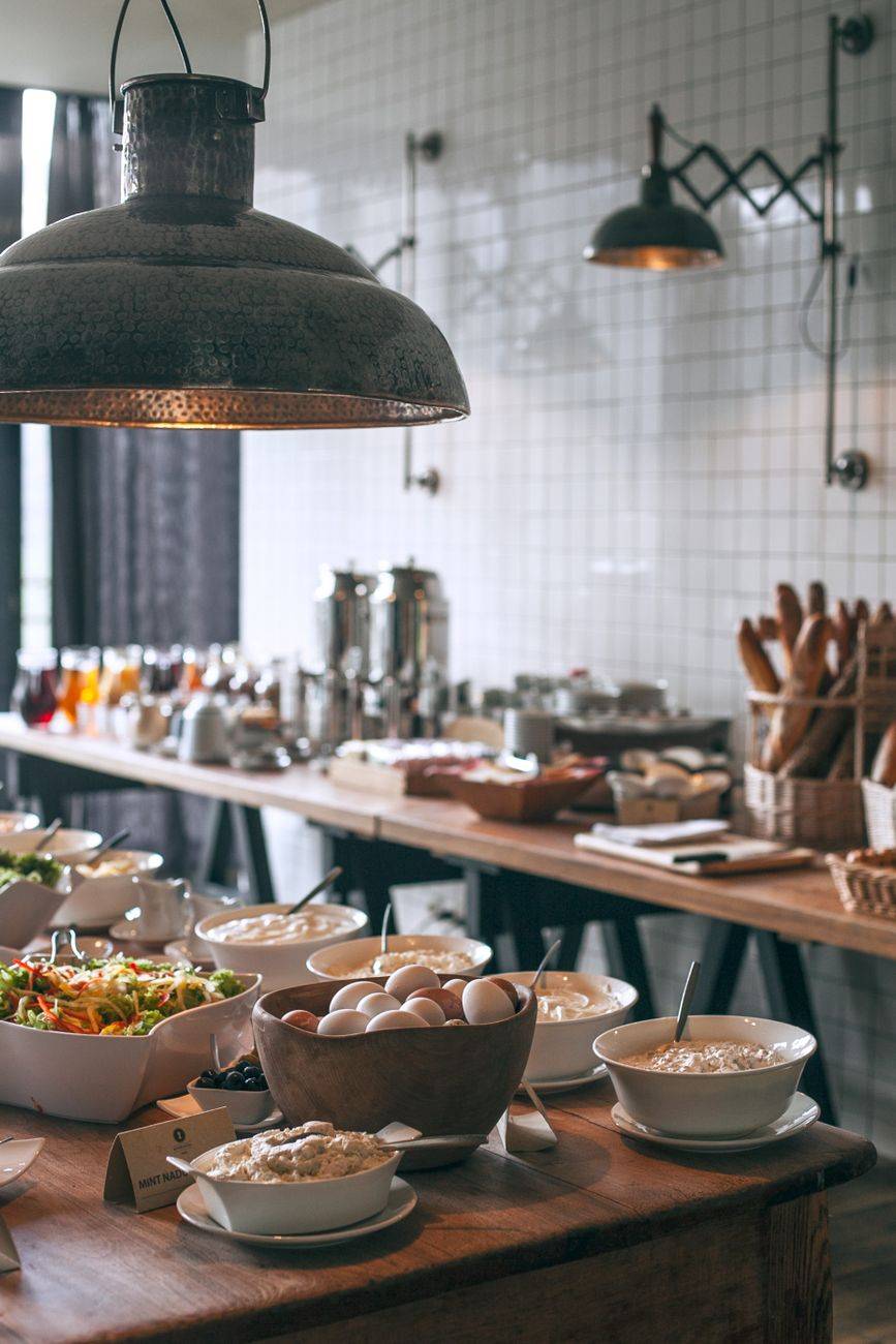 Bowls of tasty food served on banquet tables in light canteen with lamps and kitchenware and with other breakfast ingredients