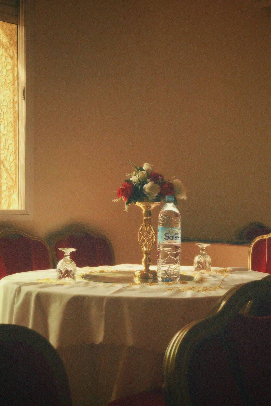 An elegantly set dining table with floral centerpiece and bottle of water in soft lighting.