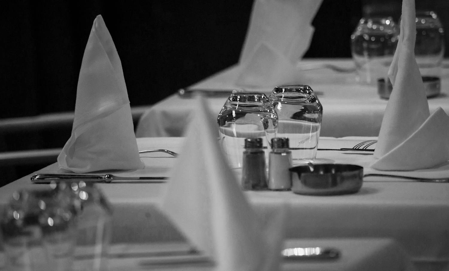 Monochrome image of a formal table setup with napkins and glassware.
