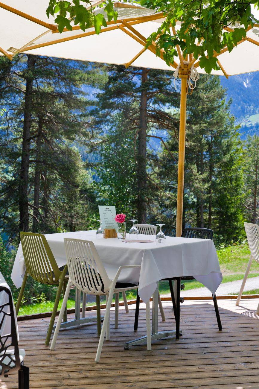 Scenic outdoor dining area amid lush alpine forest with sunlight filtering through umbrellas.