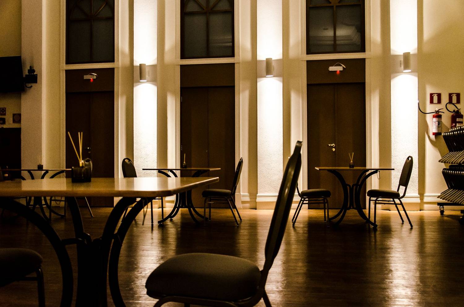 A warmly lit empty dining room with chairs and tables under soft lighting, evoking solitude.