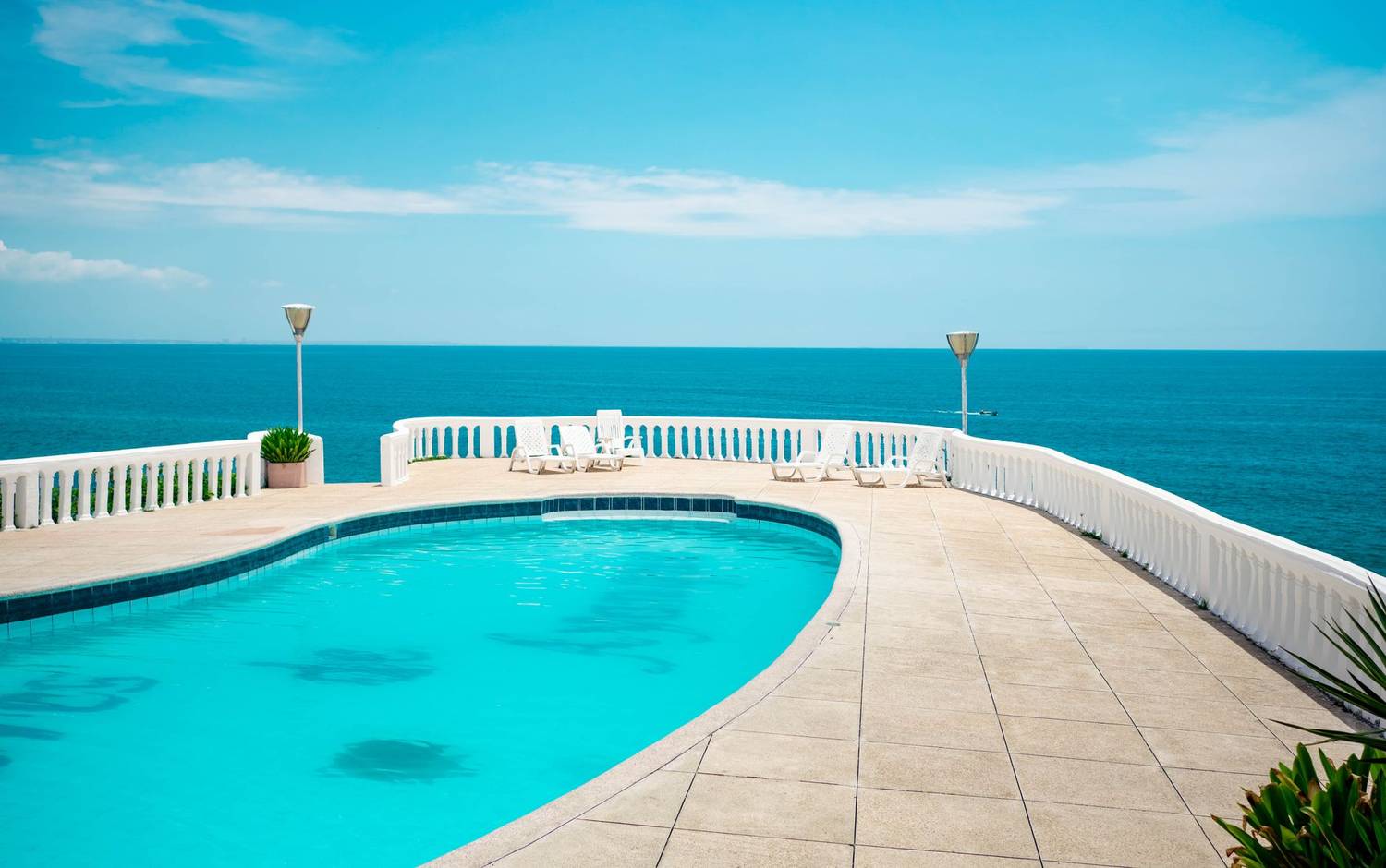 A tranquil swimming pool at a seaside resort with ocean views under a clear blue sky.