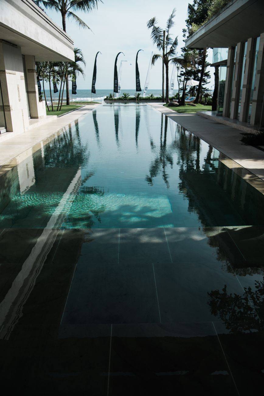 Serene infinity pool view with palm trees and ocean at a Bali resort, perfect for relaxation.