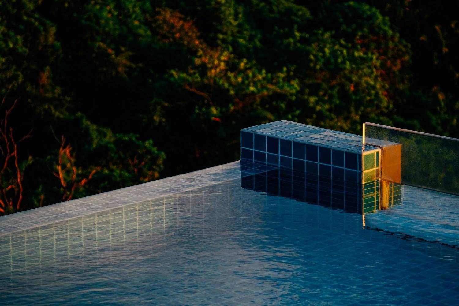 A serene poolside scene with sunset reflections and lush greenery.