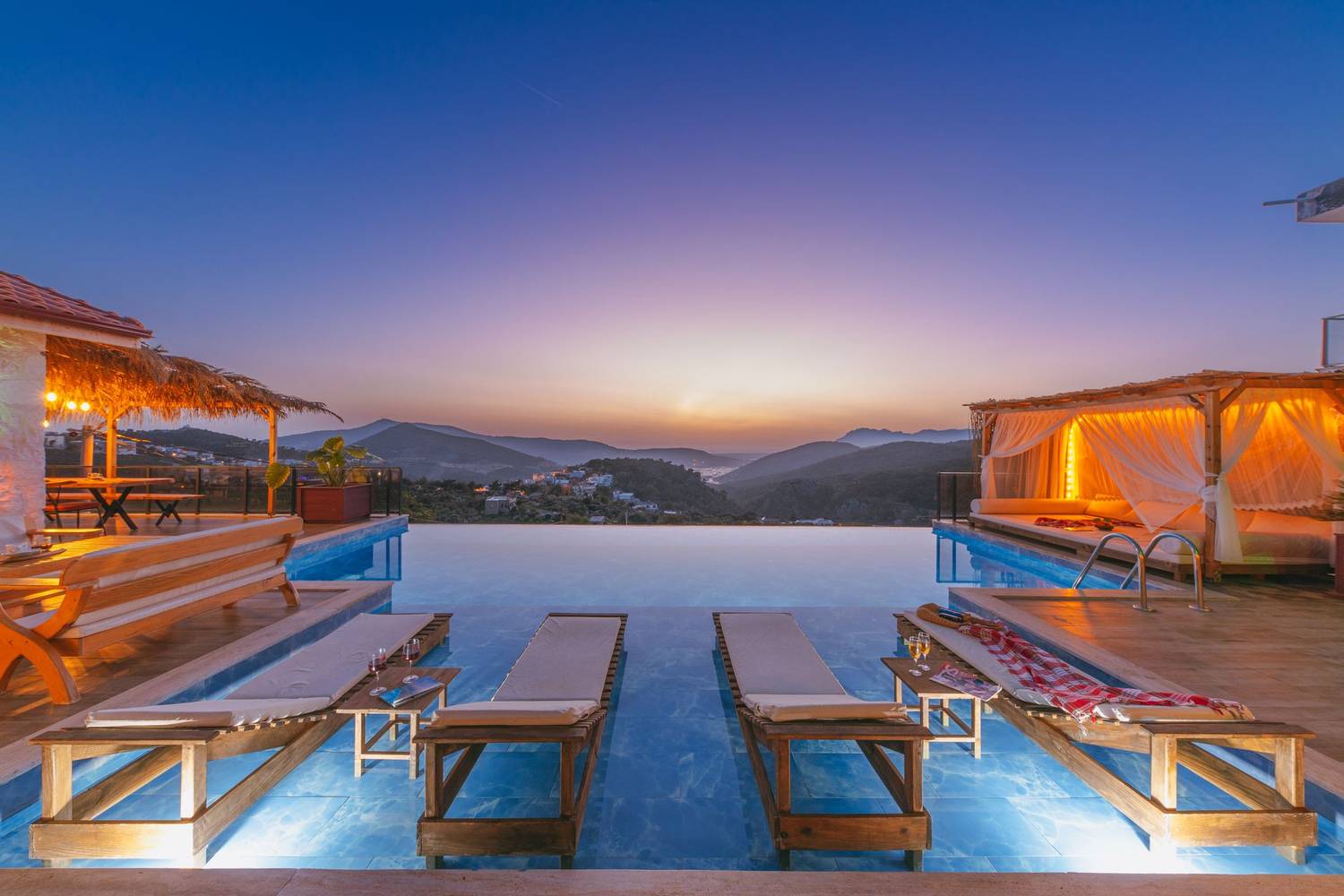 Spacious infinity pool with sun loungers and mountain views at a luxury resort during sunset.