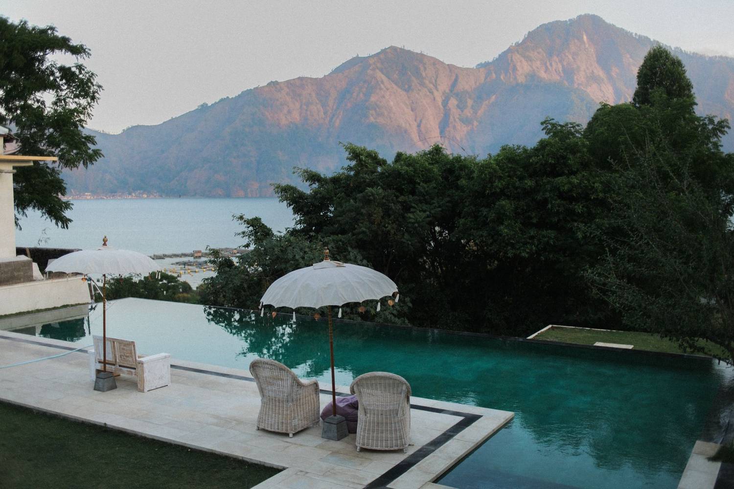 Empty swimming pool with loungers and parasols surrounded with greenery against seascape with mountanis