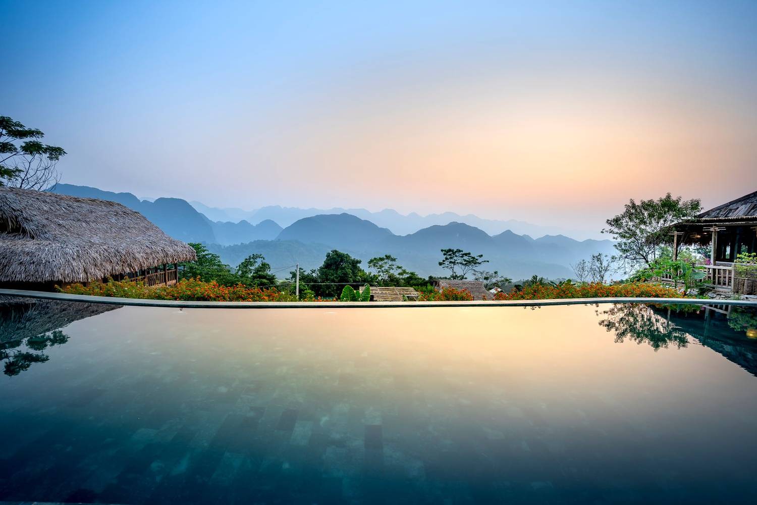 Calm water of pool located in exotic resort against wooden huts and mountainous area on evening time in tropical country