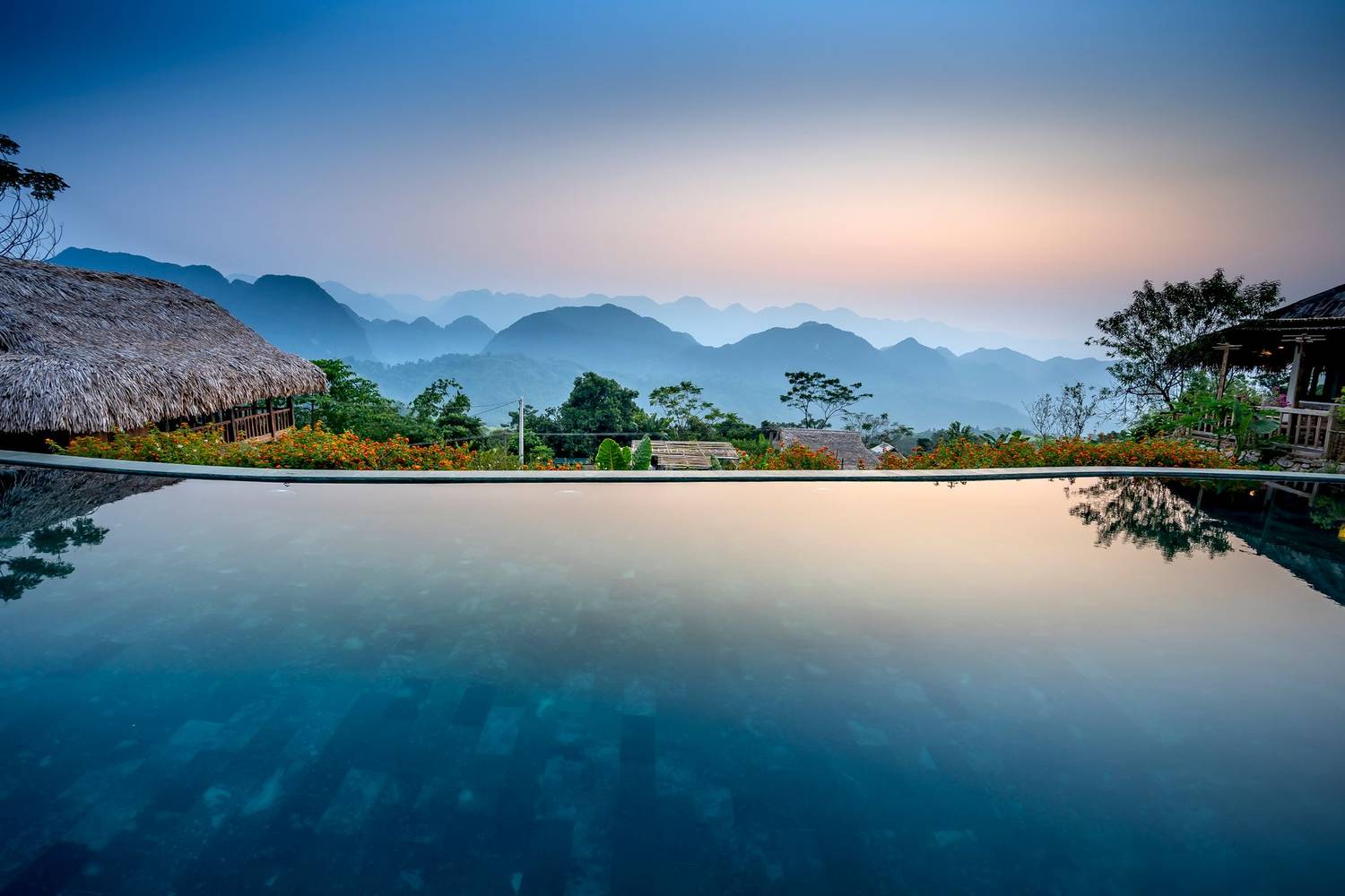 Picturesque scenery of calm blue water in pool under blue sky on sunset surrounded by lush green plants and mountains