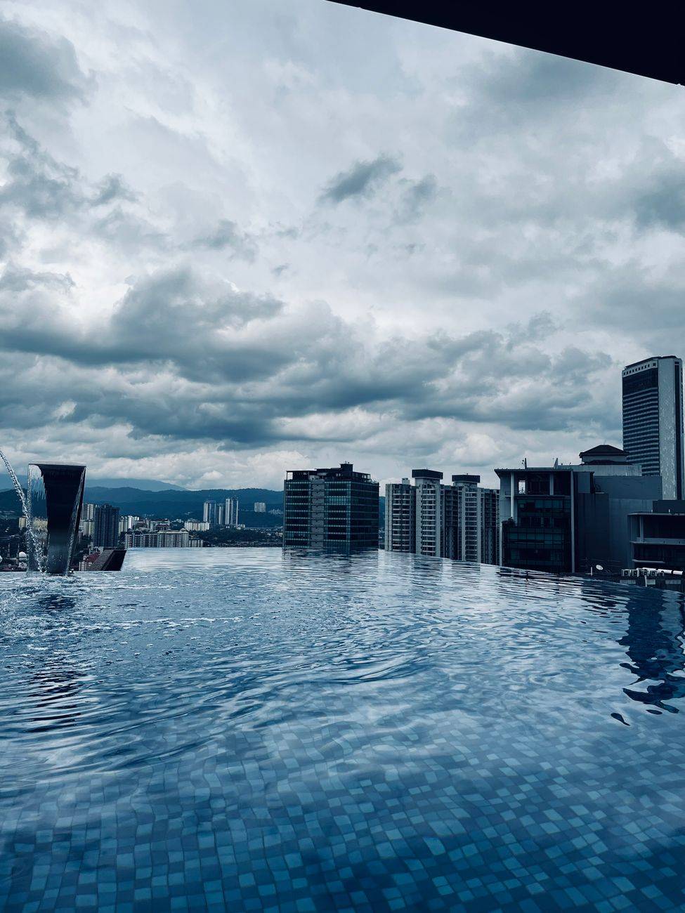 Stunning city skyline view from a modern infinity pool on a cloudy day.