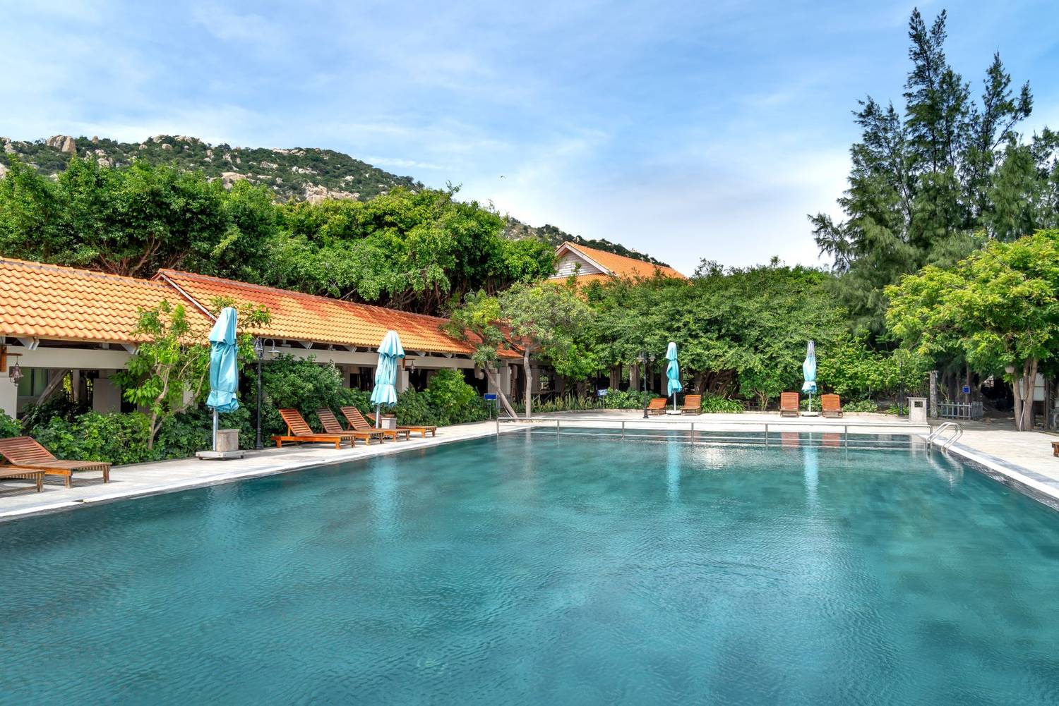Peaceful resort pool with loungers and umbrellas surrounded by greenery.
