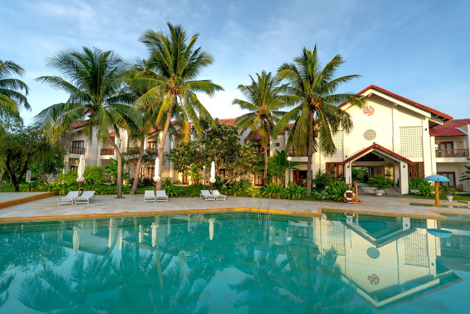 A serene tropical resort featuring palm trees and a pristine swimming pool under a blue sky.