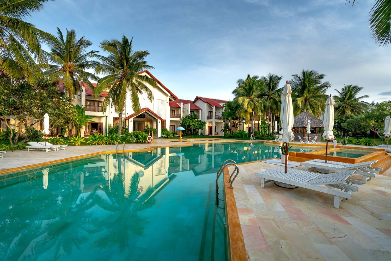 A serene view of a luxury resort with a swimming pool surrounded by palm trees.