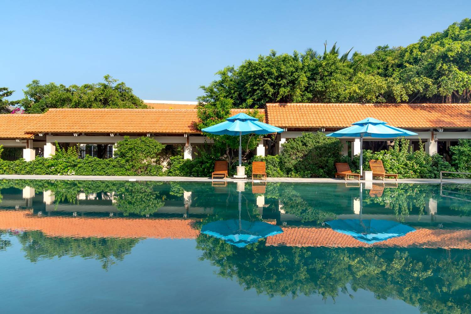 Scenic view of a resort pool with vibrant blue umbrellas and reflections, ideal for a summer getaway.