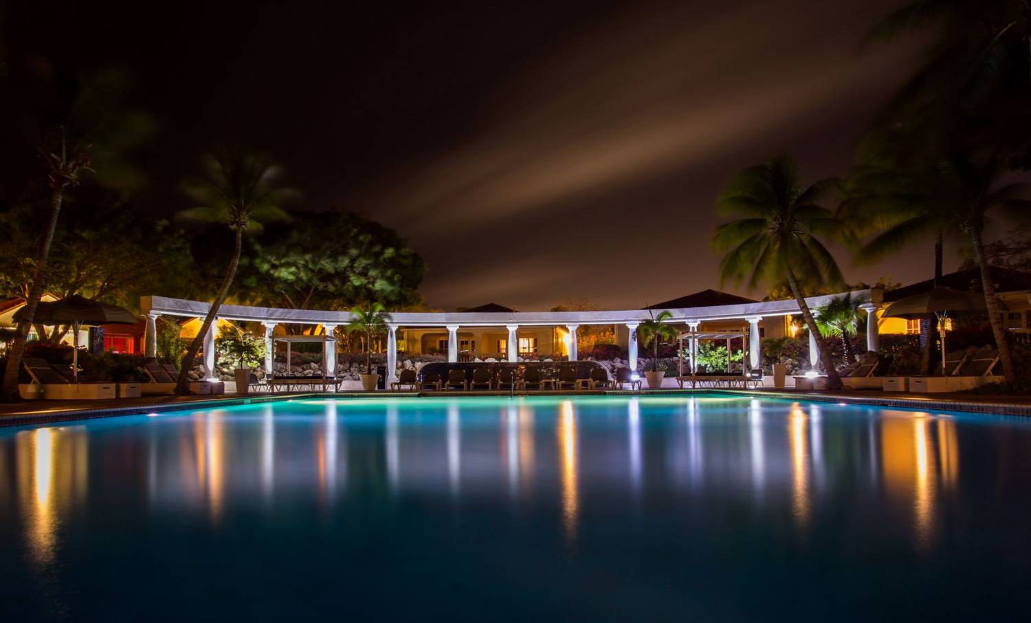 Peaceful night view of a hotel pool surrounded by palm trees and ambient lighting.