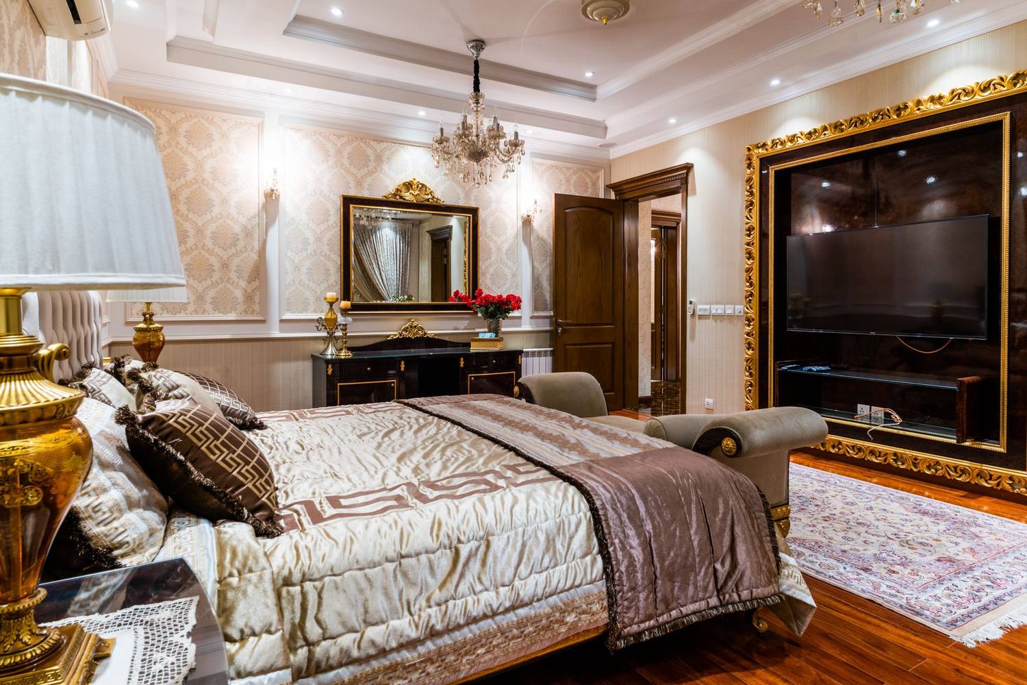 Luxurious hotel bedroom featuring elegant decor, large mirror, chandelier, and gold accents.